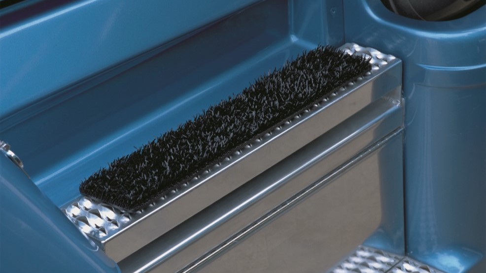a black boot mat made of fake plastic turf on top of a silver step up to the cab of a blue semi truck